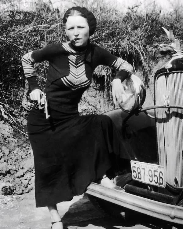 Bonnie Parker poses on her car with a cigar and a gun